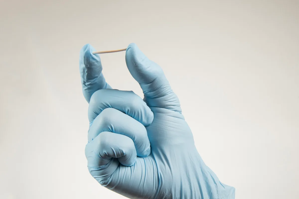 Implante hormonal segurado por mão com luva